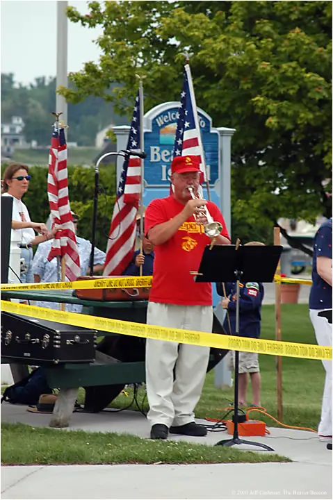 A trumpet player performs beside American flags, a music stand, and yellow barrier tape.