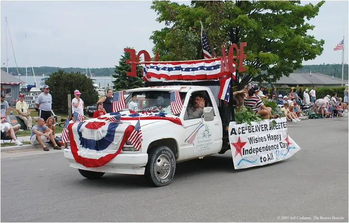 Patriotically decorated pickup truck leads a parade past seated spectators.