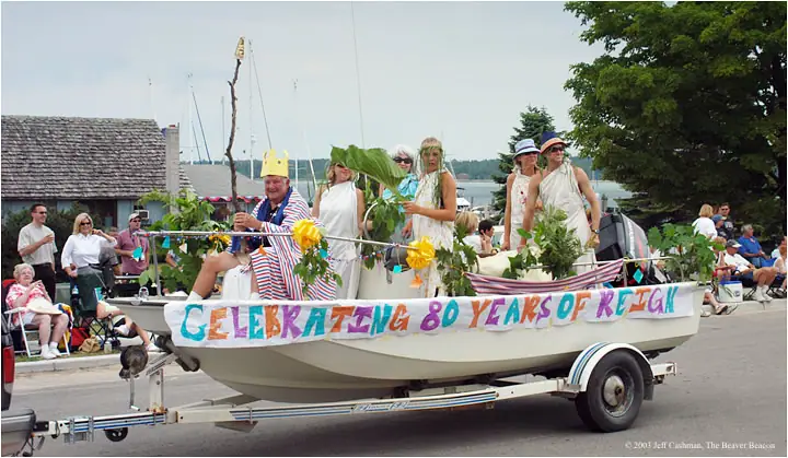 A decorated boat float carrying costumed people passes spectators on a paved street.