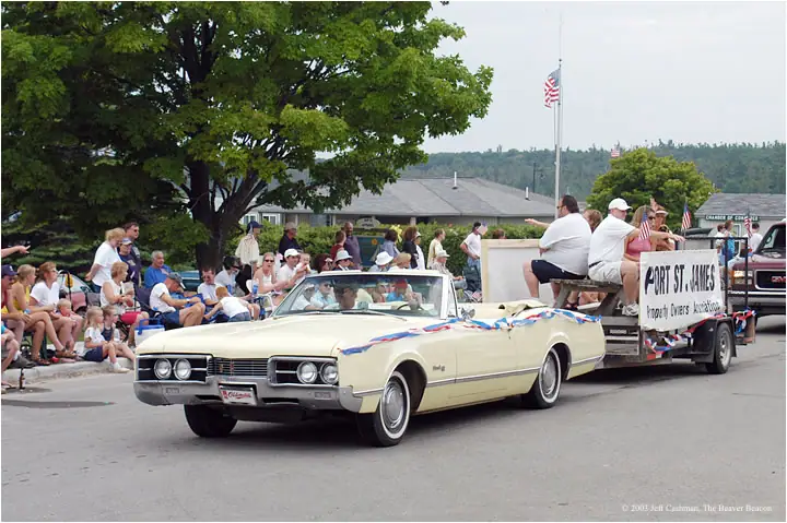 A decorated cream convertible carries people past spectators during a parade.