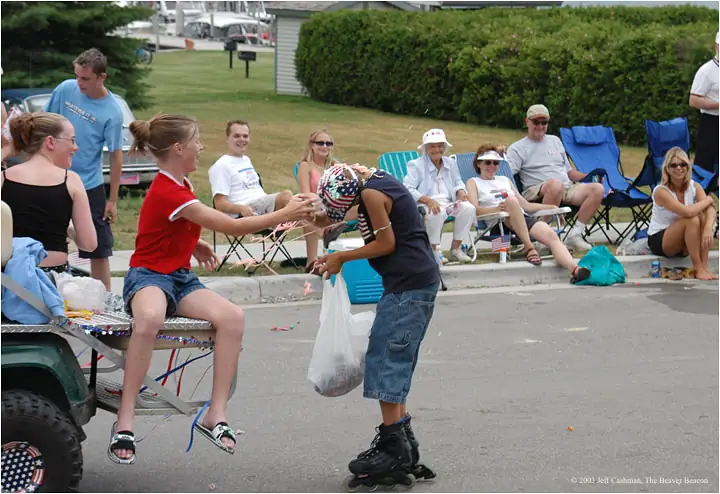 Young people exchange items beside a decorated all-terrain vehicle as spectators watch from folding chairs.