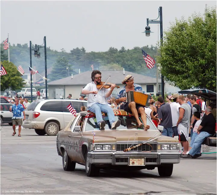Two musicians perform from the roof of a decorated sedan during a street parade.