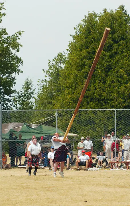 A kilted athlete throws a long wooden pole during an outdoor field competition.