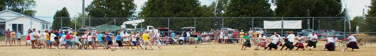 A tug-of-war contest takes place on a sandy field before a crowd of spectators.