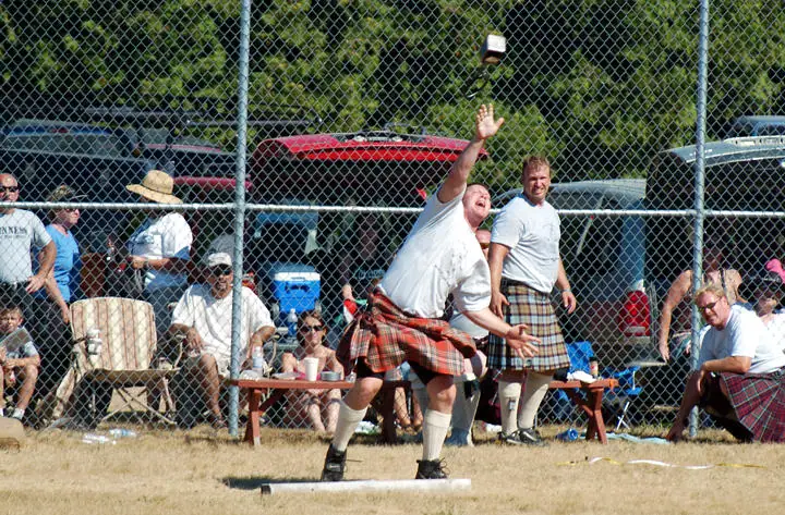 A kilted competitor throws a small object while spectators and other competitors watch.