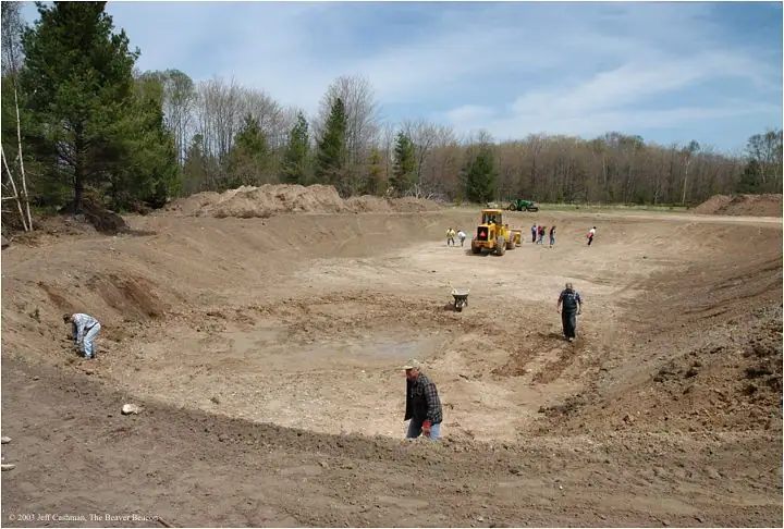 People work around a yellow backhoe in a broad, freshly excavated basin.