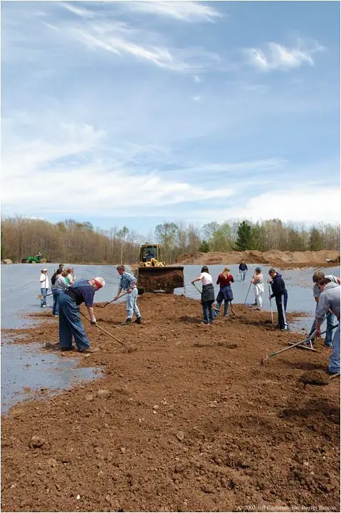 People rake wet soil in a broad excavation while a yellow bulldozer sits behind them.