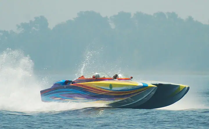 A brightly painted speedboat speeds across the water, throwing up a broad white wake.