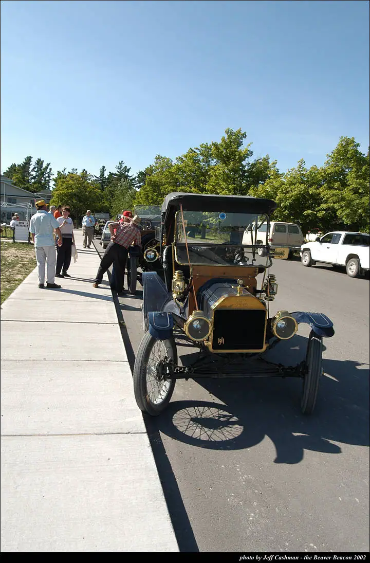 An antique automobile is displayed beside a sidewalk as people walk among parked vehicles.