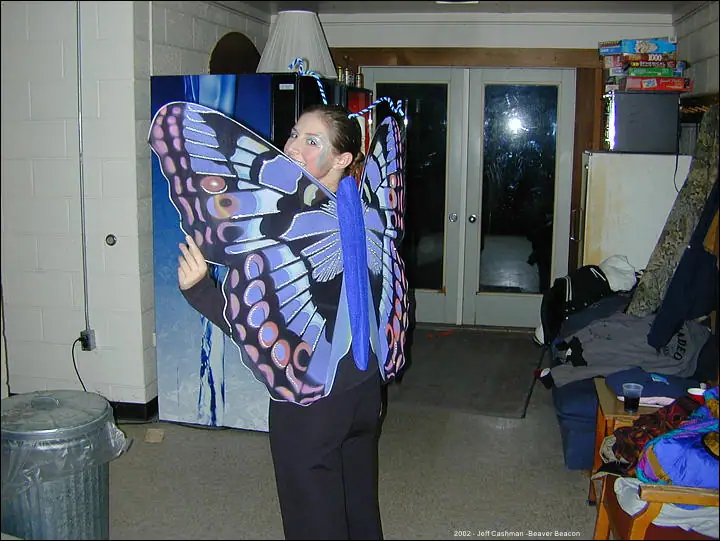 A woman displays large purple and blue butterfly wings indoors.
