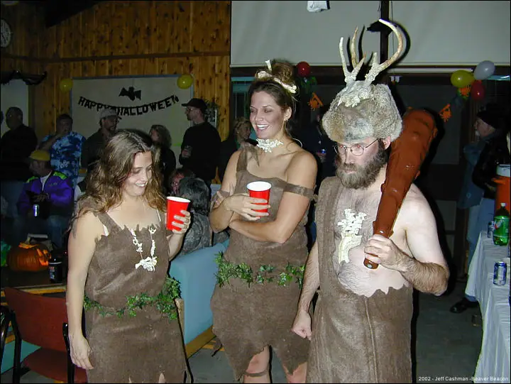 Three adults in rustic costumes pose with red cups at an indoor Halloween party.