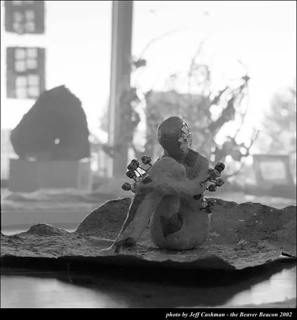 Black-and-white photograph of a small seated sculpture displayed on a rough sculptural base.