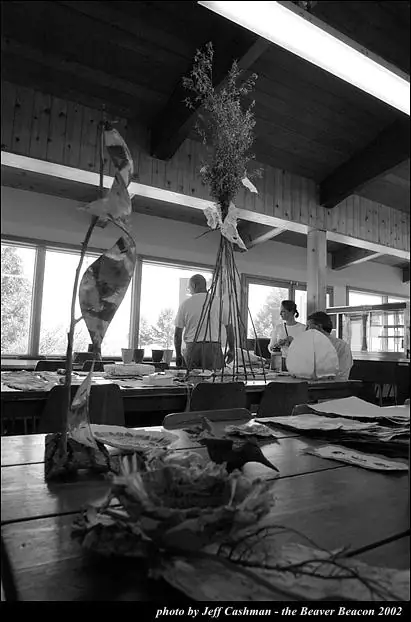 Black-and-white photograph of sculptural forms on tables in a bright room with several people.