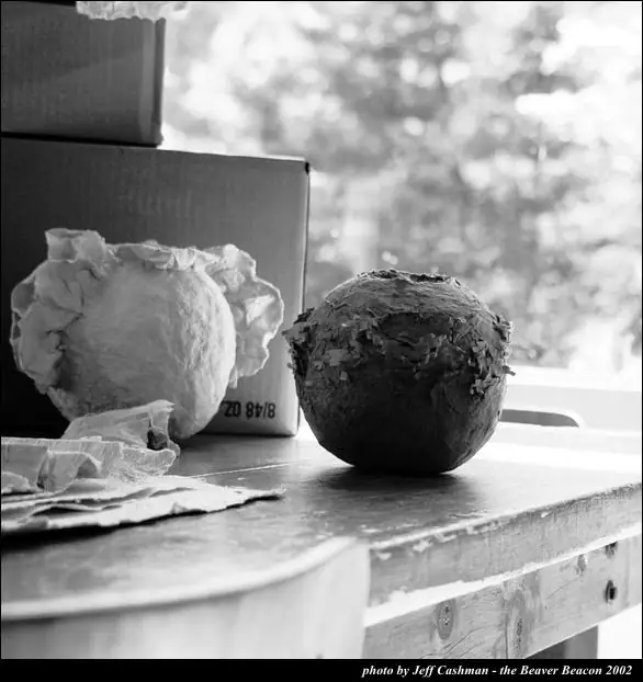 Two textured paper spheres sit on a tabletop beside cardboard boxes and loose sheets of paper.