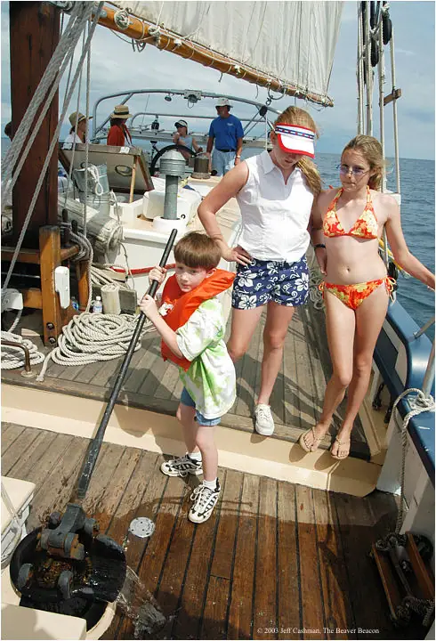 Children stand on the deck of a schooner among ropes, rigging, and deck machinery.
