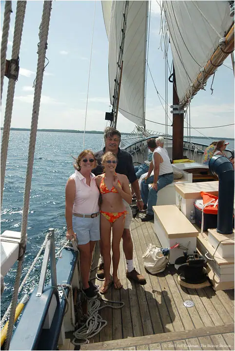 Passengers pose on the deck of a sailing vessel beneath raised sails.