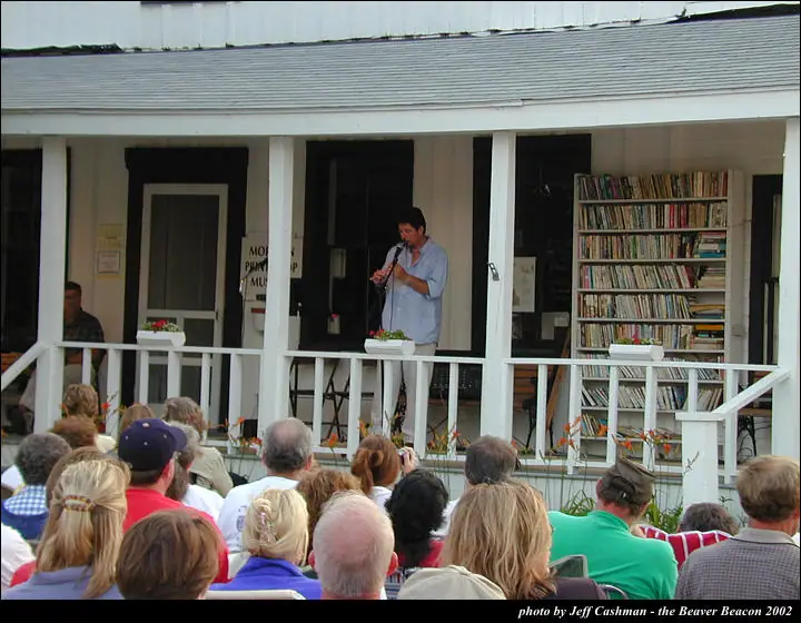A man addresses a crowd from a porch while holding a microphone.