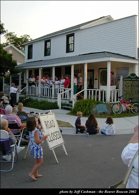 People sing on a house porch as a child holds a ROAD CLOSED sign.