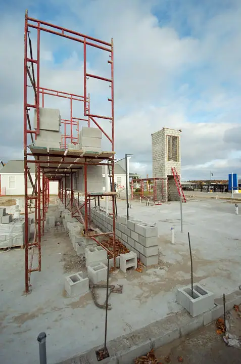 Concrete block walls and red scaffolding surround a partially built structure beneath a cloudy sky.