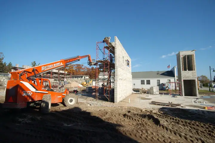 Construction site with concrete block walls, scaffolding, and an orange boom lift.