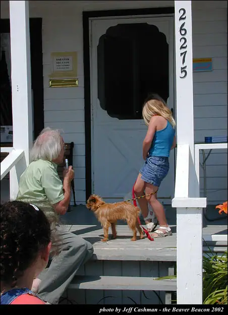 A child stands with a small dog on a porch while adults sit nearby.