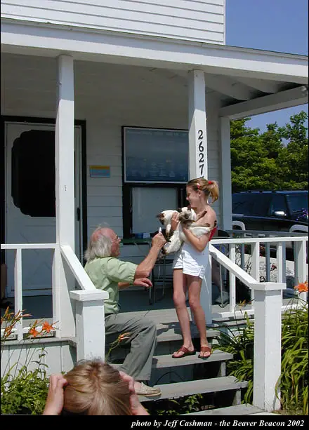 An older man and a girl handle a small white dog on the steps of a porch.