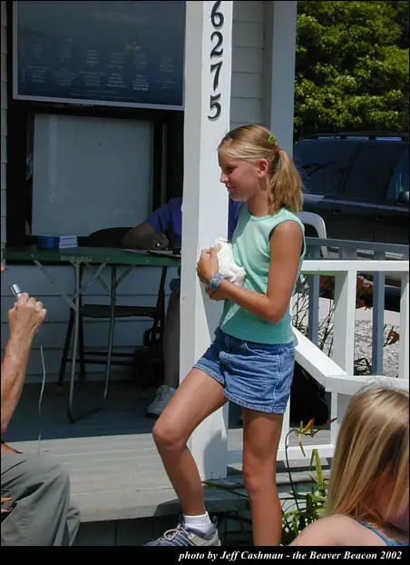 A girl carries a small white animal across a porch while people sit nearby.