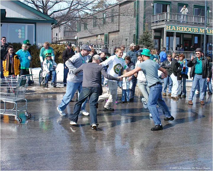 People pull against one another on a wet street beside shopping carts and a building marked “HARBOUR MAR…”