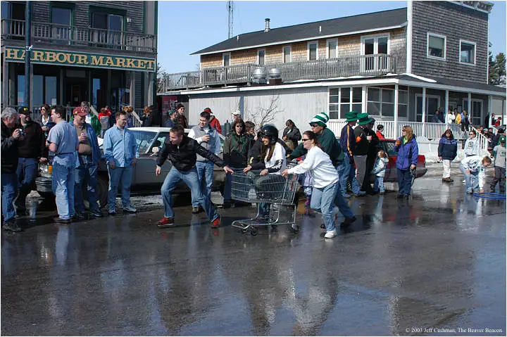 People push a shopping cart across a wet street while a crowd watches outside Harbour Market.
