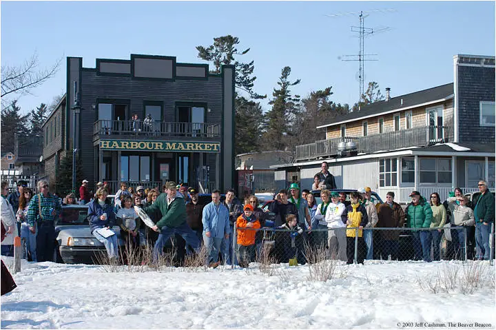 A crowd watches a runner in a snowy street outside a building marked HARBOUR MARKET.