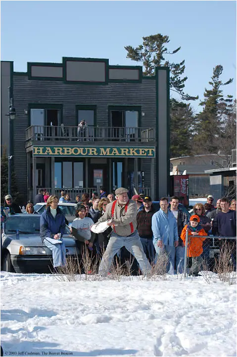 A man throws a white object across a snowy area as a crowd watches outside Harbour Market.