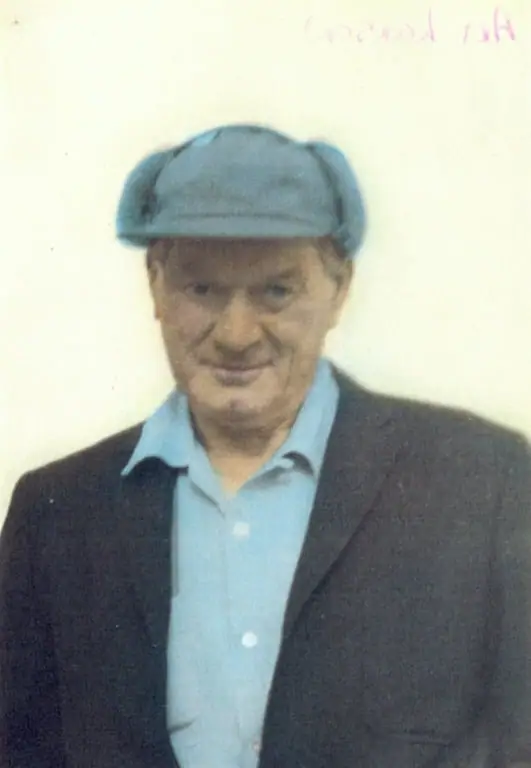 Portrait of a man wearing a blue flat cap, light blue shirt, and dark jacket.