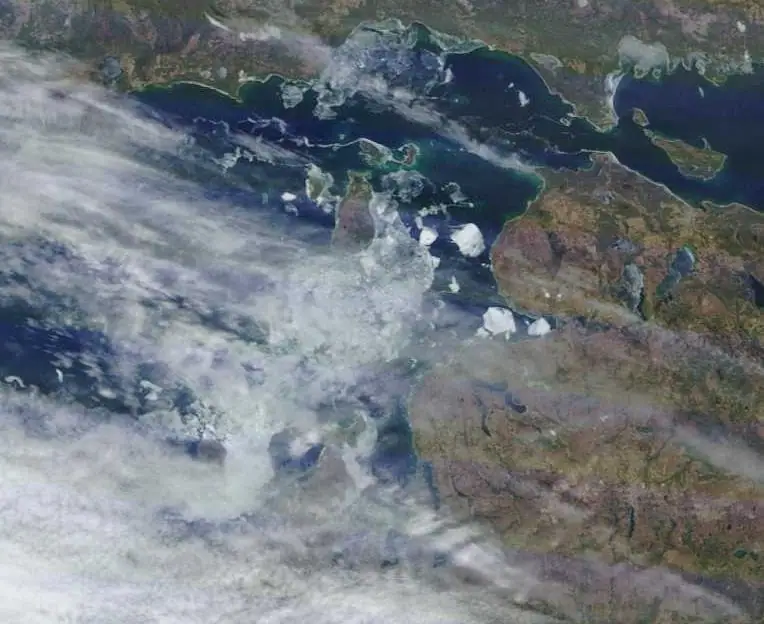 Aerial image showing dark water, surrounding land, scattered ice, and broad bands of cloud.