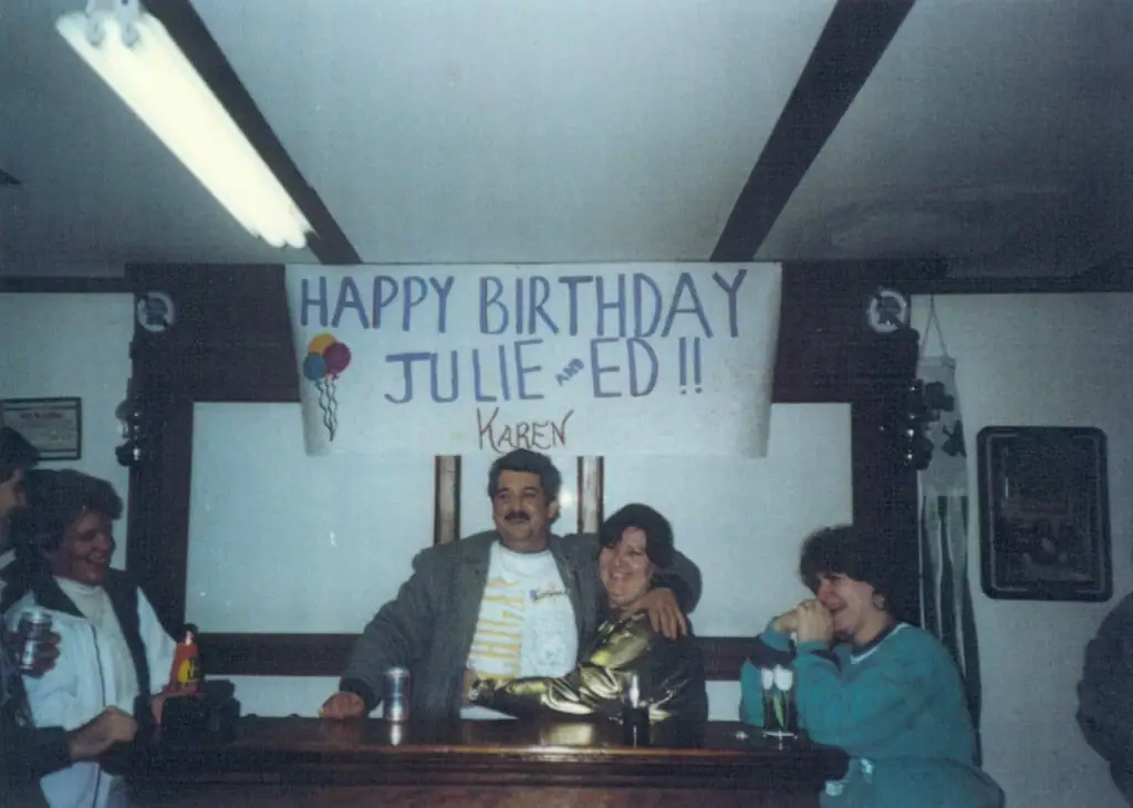 Four people gather behind a bar beneath a handmade birthday banner.