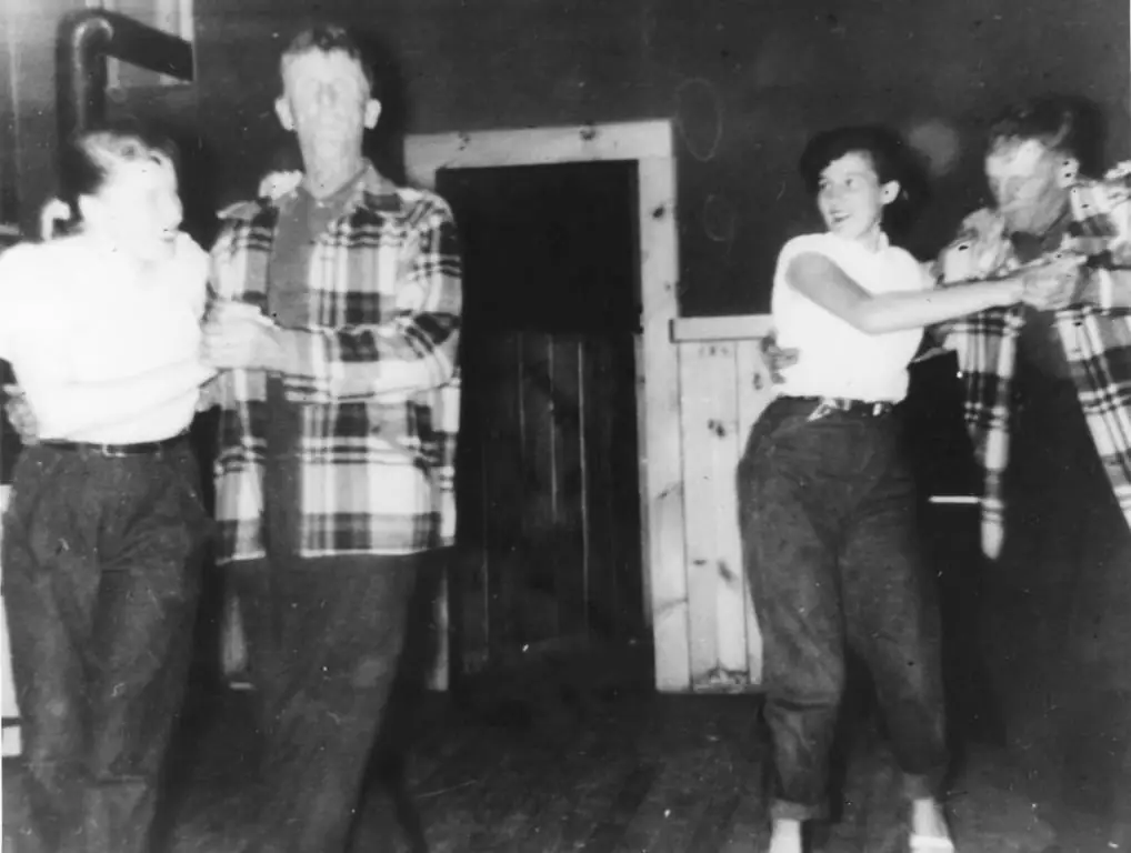 Four people dance together inside a wood-paneled room.
