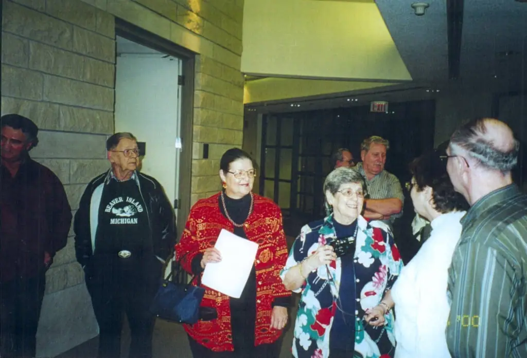 A group of adults gathers in an indoor hallway, with two people holding papers or small objects.
