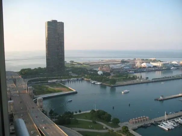 Aerial photograph of a waterfront harbor with boats, a tall tower, roads, and an amusement park.
