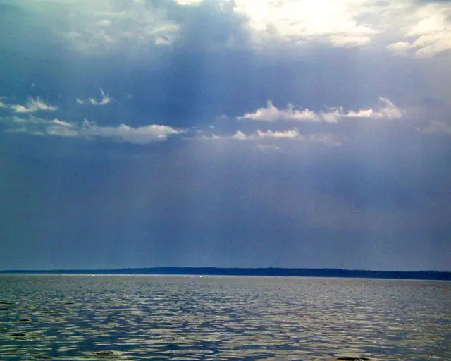 Rippling water beneath dramatic layered clouds and a dark, distant shoreline.