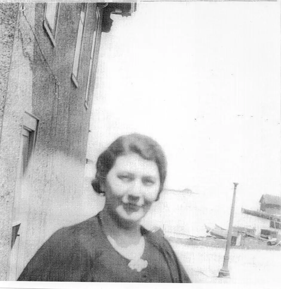 Black-and-white portrait of a woman standing beside a building with snow-covered ground behind her.