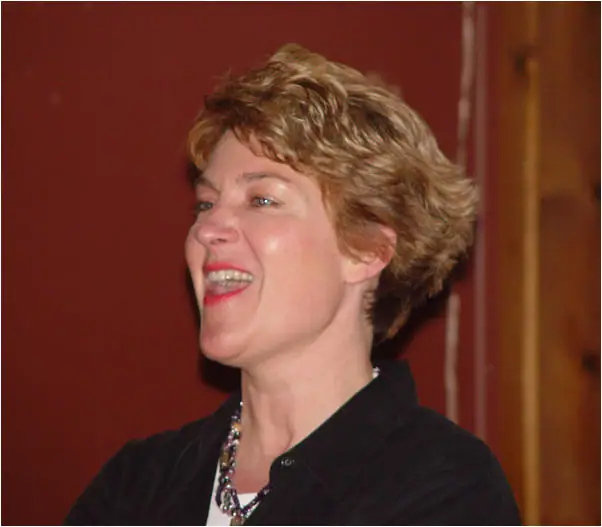 Close-up portrait of a smiling woman with short hair, a black top, and a beaded necklace.