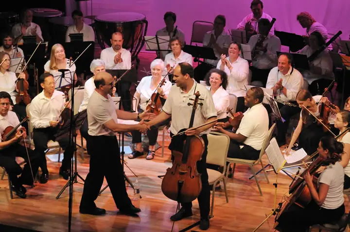 A large string ensemble performs while two men shake hands at the front of the stage.