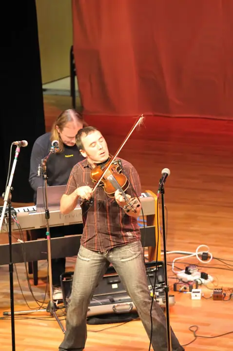 A violinist performs in front of a keyboard player on a stage.