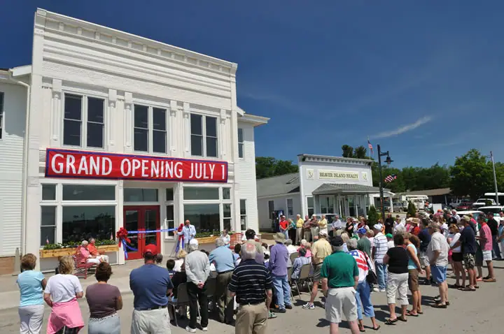 Crowd gathers outside a white commercial building for a ribbon-cutting ceremony.
