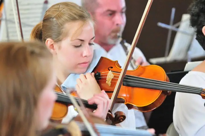 Young violinists perform together in a close-up view of a string ensemble.