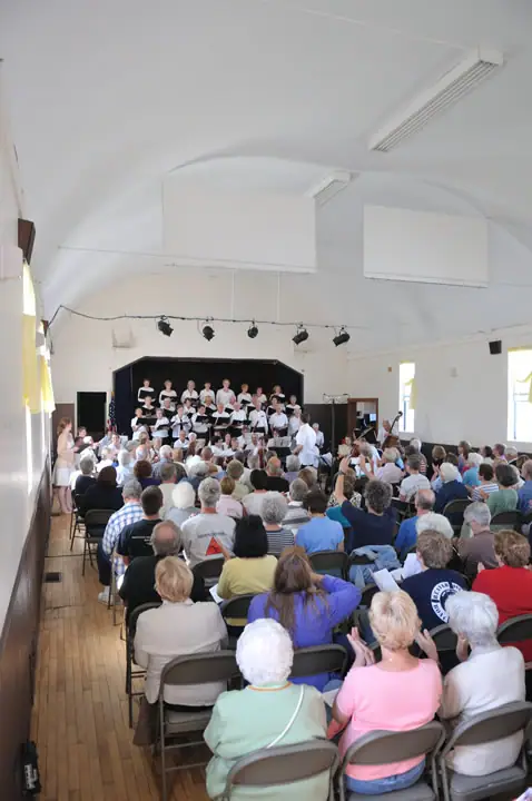 A choir and musicians perform for a seated audience in a bright hall.