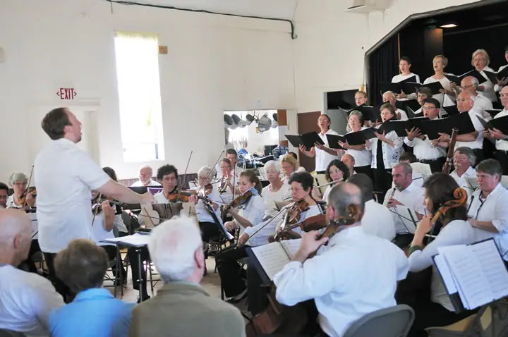 An orchestra and choir perform indoors under the direction of a conductor.