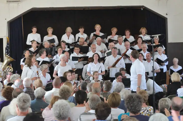 A choir and instrumentalists perform on a stage before a seated audience.