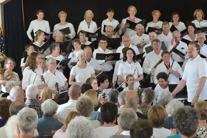 A choir and orchestra perform before a seated audience.