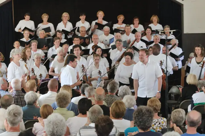A choir and string musicians perform before a seated audience.