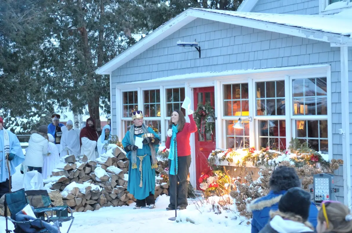 Costumed people gather outside a blue-shingled house in a snowy scene.